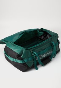 Green and black duffel bag made of durable fabric, featuring a large zippered opening, dual carrying straps, and a prominent logo on the side.