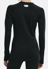 Czarna, długa koszulka sportowa z długim rękawem, wykonana z gładkiego materiału. Posiada okrągły dekolt i rękawy raglanowe. Logo Under Armour na górnej części pleców.