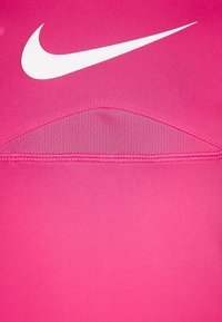 Haut de sport rose en tissu extensible avec un col rond, arborant le logo swoosh blanc de Nike et un détail texturé à l'arrière.