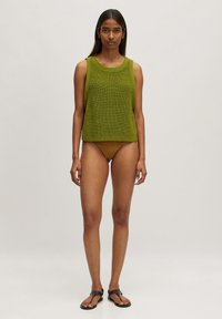 Grünes, gestricktes ärmelloses Oberteil mit rundem Halsausschnitt und strukturiertem Design, kombiniert mit einem braunen Bikinihöschen. Einfache flache Sandalen runden den Look ab.