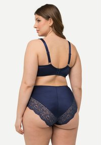 Tummansininen alusvaatesarja, jossa on ribbattu rintaliivit säädettävillä olkaimilla ja pitsireunustetut korkearajaiset alushousut, jotka korostavat yhtenäisiä yksityiskohtia.