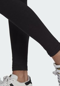 Svarta leggings av stretchigt material, figursydd design med en jämn textur, kombinerat med vita sneakers med svarta detaljer.