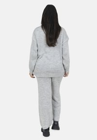 Maglione grigio a maglia con vestibilità ampia e maniche a coste abbinato a pantaloni grigi a maglia. Stivali neri con tacco alto completano l'outfit.