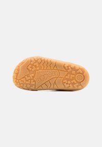 Brun gummisåle med teksturerte gripe mønstre, som har logo og størrelsesdetaljer. Ergonomisk design som passer til ulike terreng.