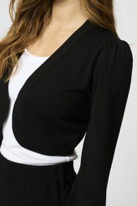 Svart croppad cardigan med ribbade kanter, långa puffärmar och en djup v-ringning, överlagd på en vit topp. Slät stickad textur.