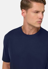 Námořnická modrá tričko s krátkým rukávem ze hladkého materiálu. Má klasický kulatý výstřih a jemné švy podél okrajů.