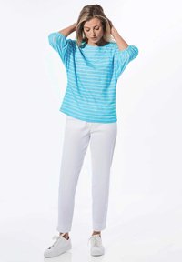 Hellblau gestreiftes Oberteil mit Dreiviertelärmeln, kombiniert mit weißen Hosen und weißen Turnschuhen. Das Oberteil hat einen lockeren Schnitt und eine weiche Textur.