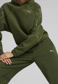 Olijfgroene hoodie met bijpassende joggingbroek. Voorzien van een Puma-logo en lichtblauwe contourdetails op de mouwen. Zachte stof met geribbelde manchetten.