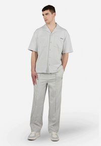 Camisa cinza-claro de manga curta com dois bolsos no peito e um tecido texturado, combinada com calças cinza-claro com riscas laterais.