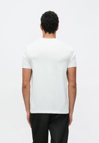 Λευκή κοντομάνικη μπλούζα με στρογγυλή λαιμόκοψη, μαλακό ύφασμα και εφαρμοστή γραμμή. Χωρίς ορατά σχέδια ή διακοσμητικά. Εμφανίζεται η πίσω όψη.