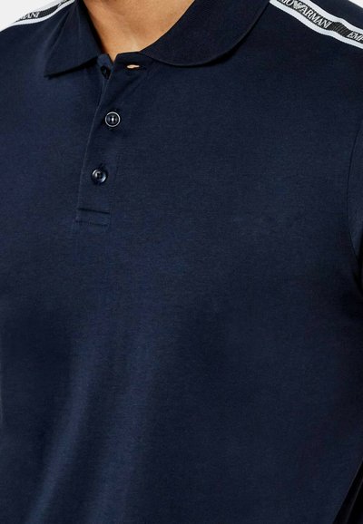 Polo shirt blu scuro con colletto classico, patta con tre bottoni e strisce bianche a contrasto con il marchio su ciascun spalla.
