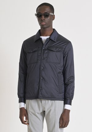 Chaqueta puffer azul marino con cuello solapa, dos bolsillos en el pecho y botones a presión. Combinada con pantalones de tejido gris claro. Tela texturizada.