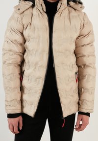 Beige padded jacket with a textured finish, zip closure, and hood. Red accents on the zipper, featuring elastic cuffs and side pockets.