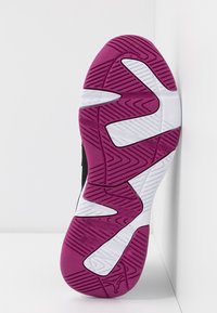 Suola di una scarpa sportiva con un battistrada a motivi viola e bianchi, poggiata verticalmente contro un angolo bianco tra parete e pavimento.
