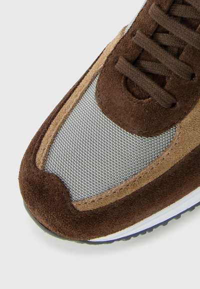 Brown suede and beige mesh sneaker toe with brown laces and white sole, shown on white background.