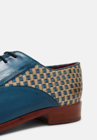 Chaussure habillée en cuir bleu avec un panneau en cuir tissé beige et un talon en bois brun, vue de côté arrière.