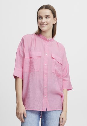 Chemise rose à manches courtes avec col mandarin, deux poches poitrine et finition texturée. Fermeture à boutons sur le devant et coupe ample.