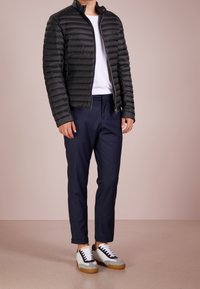 Svart vadderad jacka, vit t-shirt, marinfärgade byxor och grå/svarta sneakers. Anmärkningsvärd horisontell quiltning på jackan, med dragkedjestängning.