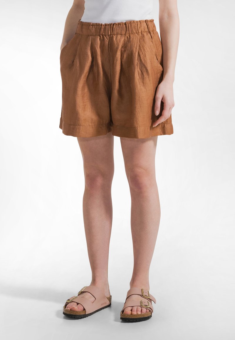 Brązowe lniane szorty o fakturowanym wykończeniu, z elastycznym pasem, przednimi kieszeniami i luźnym krojem. W zestawieniu z jasnoróżowymi sandałami.