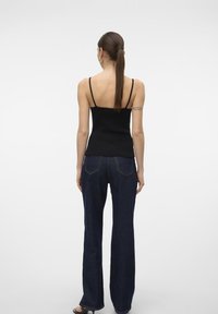 Czarny żebrowany top na ramiączkach, dopasowany do ciemnoniebieskich rozszerzanych dżinsów. Charakteryzuje się gładką teksturą i klasycznym fasonem dżinsowym.
