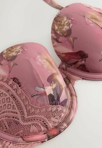 Pink floral padded bra with lace trim placed on a white surface, showing detailed stitching and fabric texture.