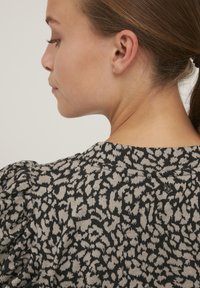 Sort og grå sweater med en tekstureret leopardprint, der har pufærmer og en knapdetalje i nakken bagpå.