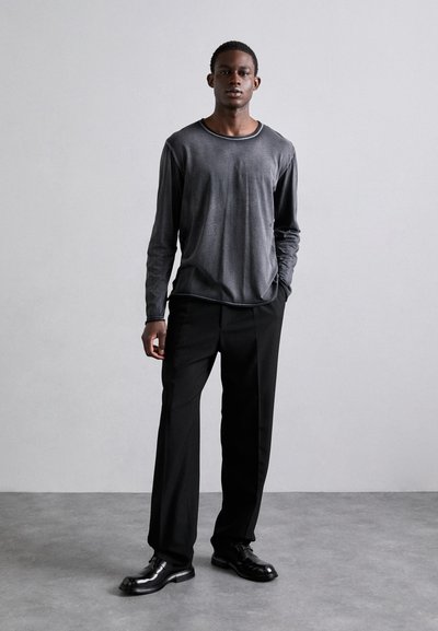 Camisa cinza de manga longa com decote redondo, combinada com calças pretas e sapatos pretos brilhantes. Design simples e ajustado, com detalhes mínimos.