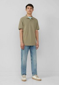 Olivgrünes Polohemd mit Kragen, kombiniert mit hellblauen Jeans und beigen Sneakern. Schlichtes Design, kurze Ärmel, keine sichtbaren Muster.