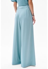 Pantalons palazzo bleu clair en tissu doux, dotés d'une taille ajustée et de deux poches arrière, avec une texture lisse et des lignes épurées.