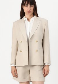 Beige dobbeltradet blazer med gullknapper, lett lin-tekstur og en enkelt brystlomme, kombinert med matchende skreddersydde shorts.