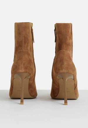 Brązowe zamszowe botki za kostkę z szpiczastym czubkiem i smukłym, wysokim obcasem. Posiadają boczny zamek i gładką teksturę na powierzchni.