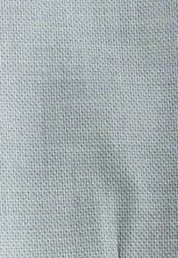 Ljusgrått tyg med ett litet, upprepat geometriskt vävt mönster som skapar en texturerad yta.