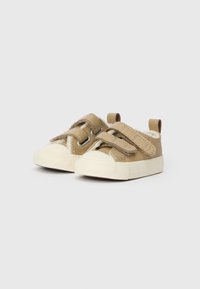 Brūni sporta apavi ar divām Velcro siksnām, noapaļotiem pirkstiem, baltām gumijas zoleēm un mīkstu iekšējo tekstūru. Mazs papēdis aizmugurē.