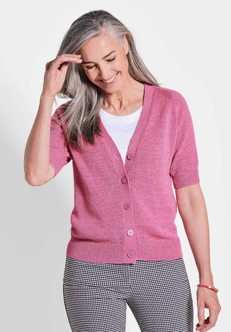 Rosa Kurzarm-Cardigan mit V-Ausschnitt, Knopfschluss und geripptem Saum. Kombiniert mit schwarz-weißen karierten Hosen.