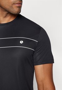 Camiseta atlética negra de manga corta, con un tejido texturizado y rayas horizontales blancas. Logo pequeño situado en la parte superior del pecho.
