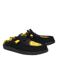 Scarpe slip-on nere con grafica di faccina sorridente gialla, dotate di una parte superiore in tessuto morbido, lacci elastici e suola in gomma testurizzata.