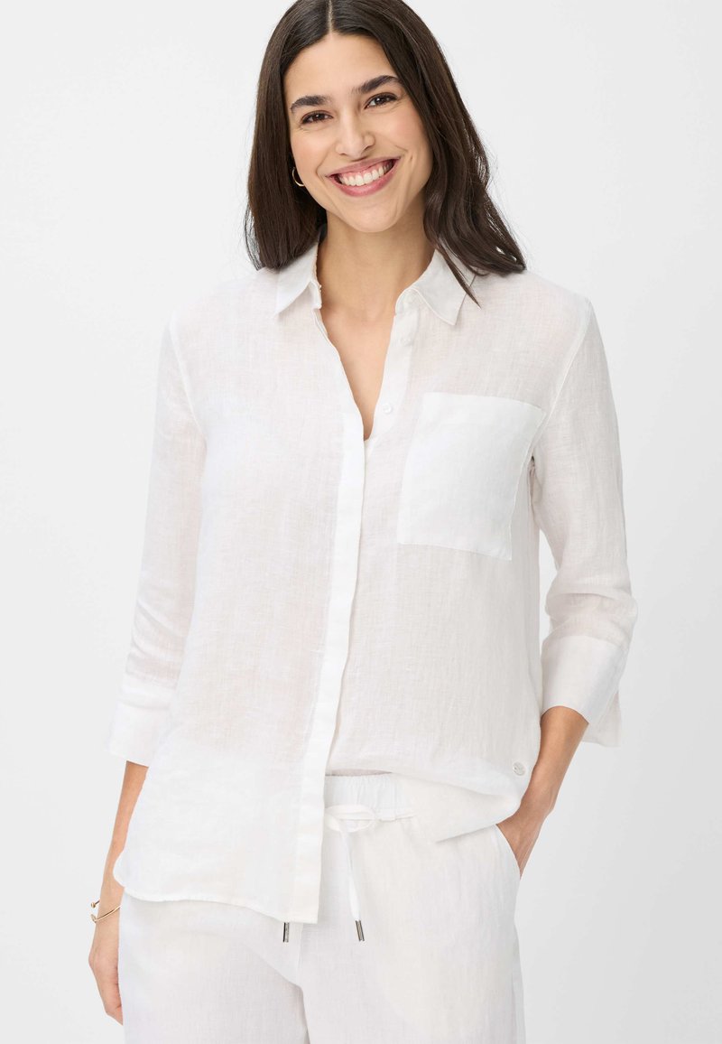 White linen button-up shirt with a single chest pocket, three-quarter sleeves, and a relaxed fit. Smooth texture, light and breathable material.