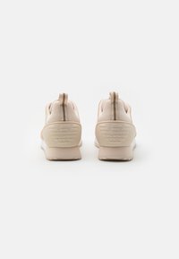 Light beige sneakers with textured fabric, padded collar, and rubber sole. Features a logo at the heel and a rear pull tab for easy wear.
