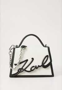Balta ir juoda rankinė su struktūruota forma, išsiskirianti ryškiu juodu "Karl" logotipu, grandinėlės dirželiu ir faktūruota paviršiaus tekstūra.