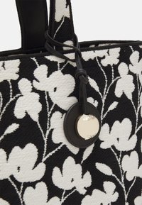 Czarna i biała torba na ramię w kwiatowy wzór z teksturowanej tkaniny, z czarnymi ramiączkami oraz okrąłym metalowym akcentem.
