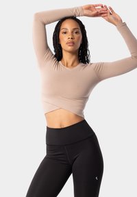 Bežs īsais garais piedurknes tops ar vortēšanas priekšpusi, apvienots ar augsto vidukļa melnajiem legingiem, kuriem ir minimāla šuvju un logo dizaina izstrāde.