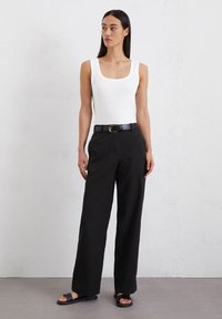 Witte mouwloze top met een vierkante halslijn, gecombineerd met hoge zwarte wijde broeken en een zwarte riem met een gouden gesp.