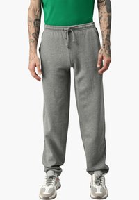 Graue Jogginghose mit elastischem Bund und Kordelzug, lockerer Schnitt und Bündchen an den Knöcheln, kombiniert mit grauen und weißen Turnschuhen.