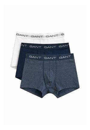 Trois paires de boxers pour hommes en blanc, bleu marine uni et bleu marine à pois blancs, chacun avec une ceinture marquée GANT.
