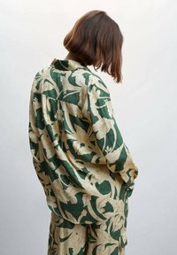 Chemise à motifs floraux verts et beiges en tissu léger, dotée d'un col et d'une coupe décontractée, vue de dos.