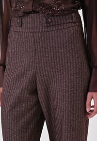 Bruine broeken met een zigzagpatroon en een hoge taille, voorzien van twee knopen en zijzakken, gemaakt van gestructureerde stof.