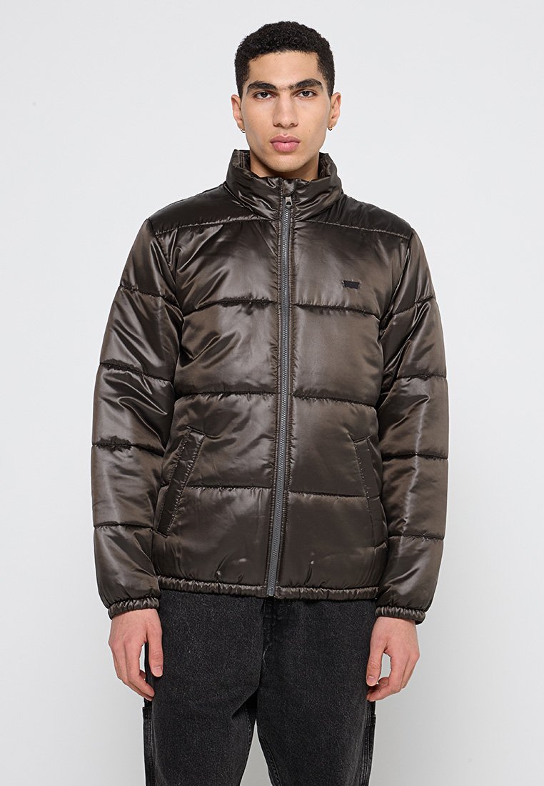 Giubbotto imbottito di colore verde oliva scuro, con colletto alto, zip frontale e polsini elasticizzati. Texture liscia e lucida con design imbottito.