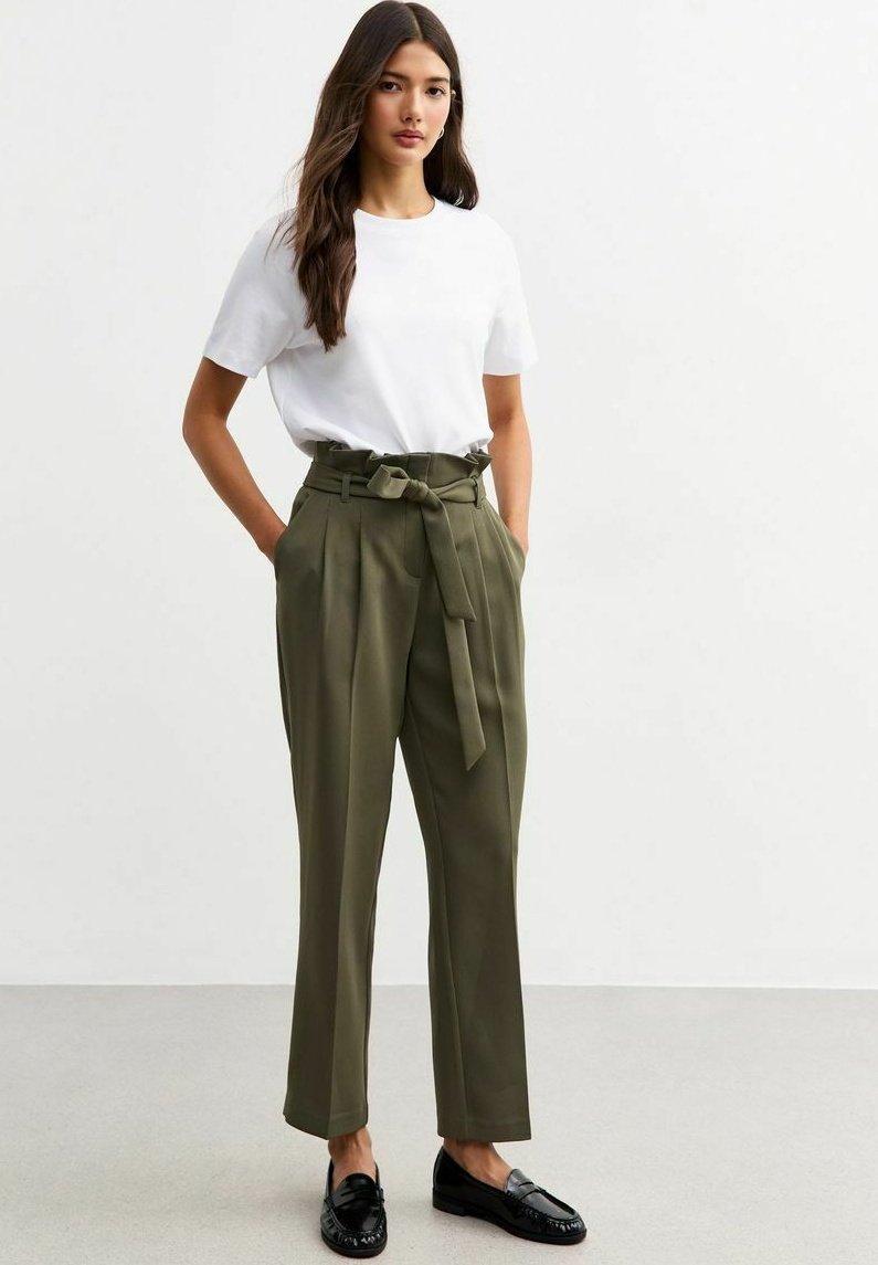 T-shirt blanc à manches courtes associé à un pantalon taille haute vert olive avec une ceinture à nouer, complété par des mocassins noirs.