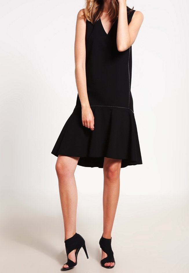 Vestido negro sin mangas con escote en V, falda acampanada y detalles de costura en contraste. Llevado con unos tacones negros de punta abierta.