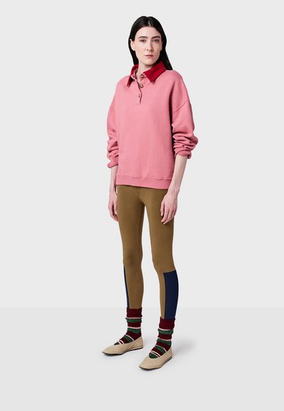 Rosa tröja med röd krage och knapppdetalj, kombinerad med bruna leggings med blå sidopaneler och mönstrade strumpor med beige skor.